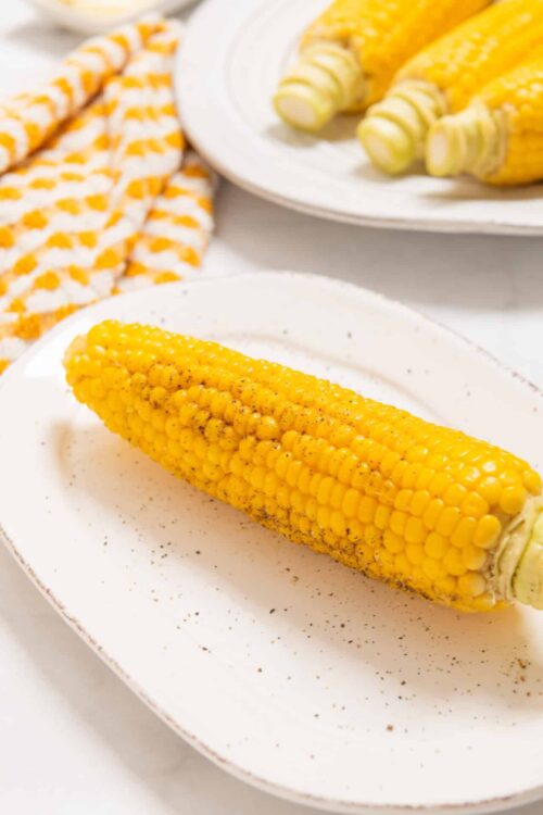 Golden roasted corn on a white plate with black pepper and seasoning.