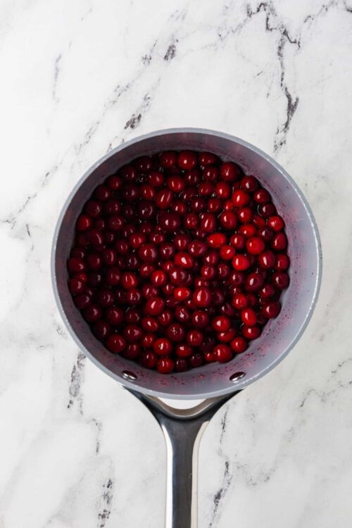 Fresh red cherries in a stainless steel saucepan on marble surface.