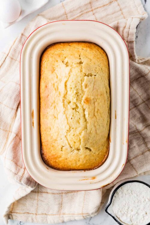 Fluffy homemade cornbread in a white baking dish on a checkered cloth.