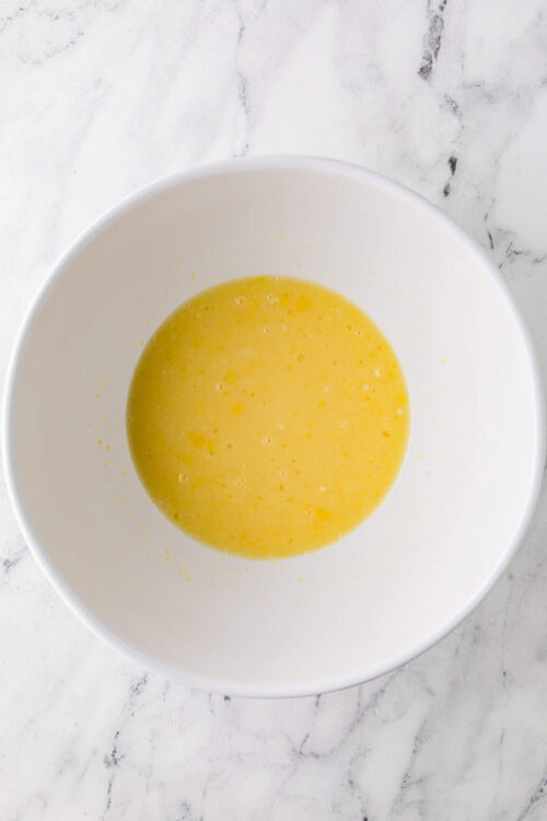 Light yellow beaten eggs in a white bowl, ready for baking or cooking.