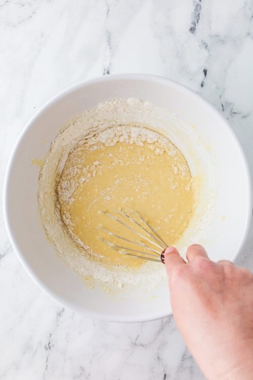 Flour and wet ingredients mixture in a white bowl with a hand whisk.