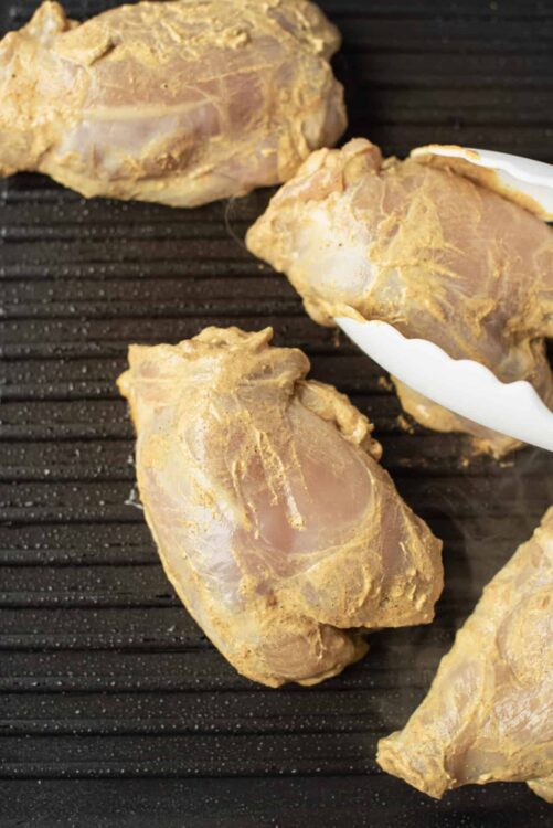 Raw chicken thighs marinated with turmeric on a black grilling pan.