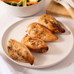 Juice chicken breasts with herbs on a white plate, served alongside a fresh vegetable salad.