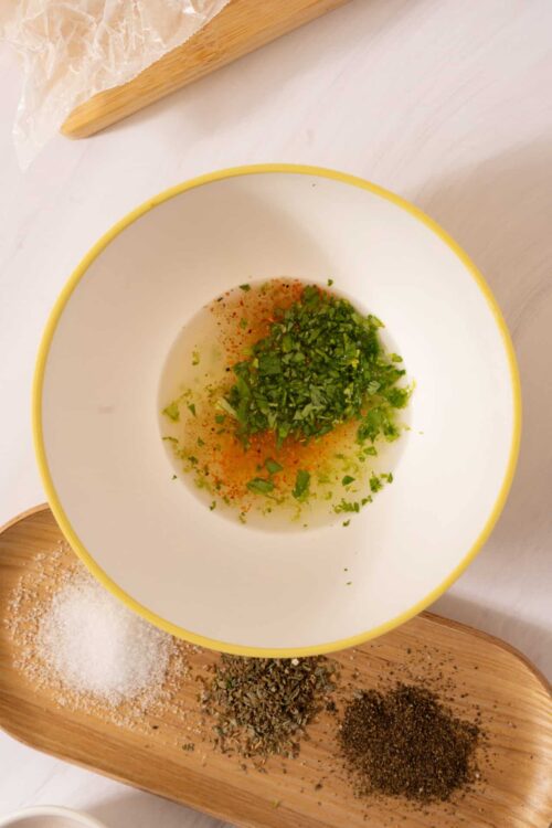 Minced herbs and spices in a white bowl for cooking or seasoning.