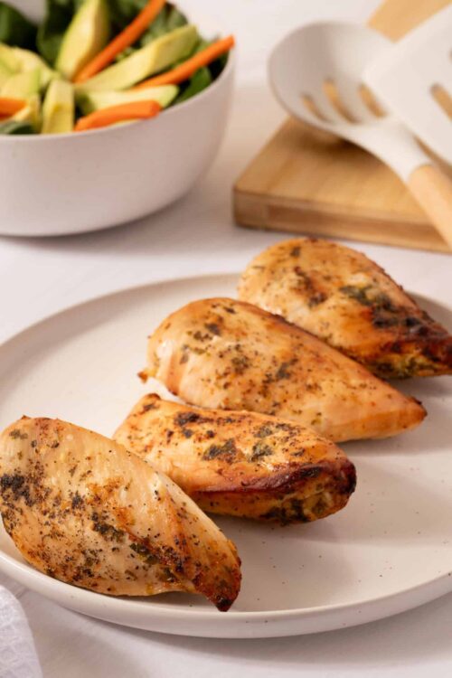 Roasted chicken breasts with herbs and spices on white plate.