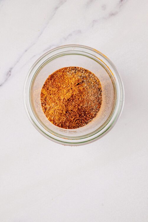 Ground cinnamon in glass jar on white marble surface.
