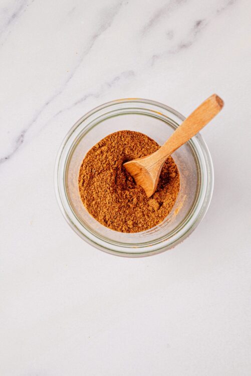 Ground cinnamon in glass jar with wooden spoon, baking spice, baking ingredients, cinnamon for recipes, baked goods, warm flavors.