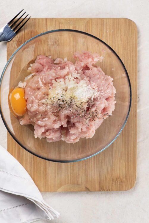 Seasoned ground chicken and pork mixture in a glass bowl for meatloaf recipe.