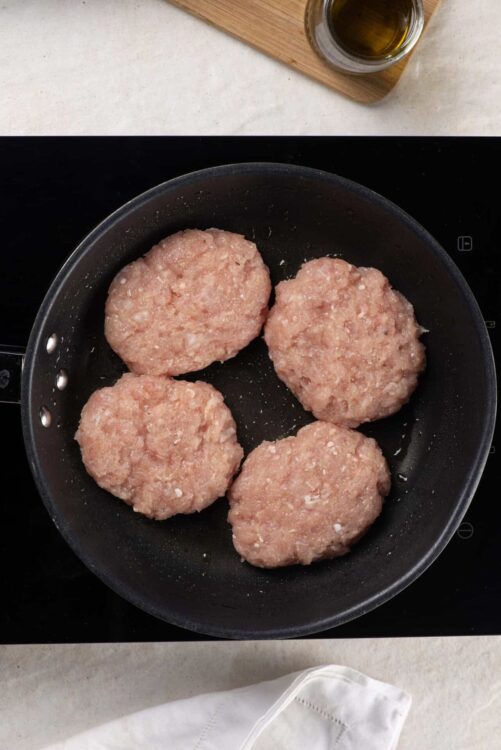 Juicy homemade sausage patties cooking in a black skillet on a modern stovetop.