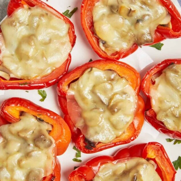 Roasted red peppers stuffed with cheese and mushrooms, baked and served on a white plate.