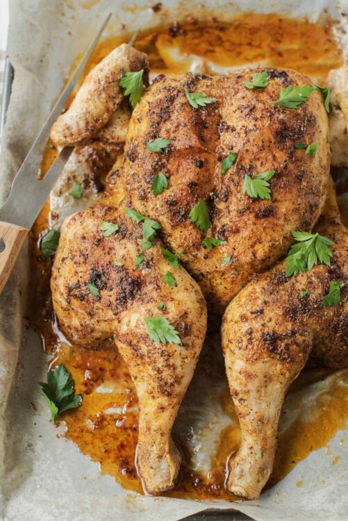 Golden roasted chicken legs with crispy skin, garnished with fresh parsley, on baking sheet.
