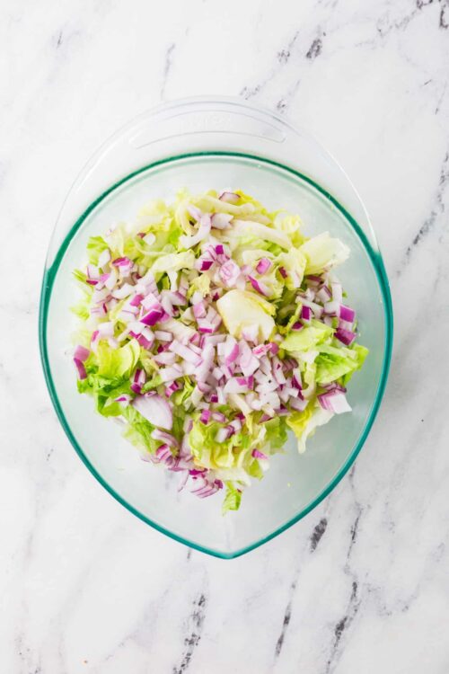 Finely chopped lettuce and red onions in a clear glass bowl for fresh salad.