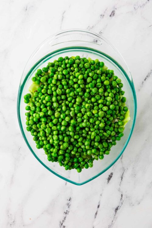 Fresh green peas in a glass bowl on a white marble surface.