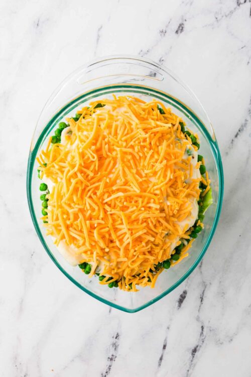 Baked Bree cheesy green pea casserole with shredded cheese in glass baking dish.