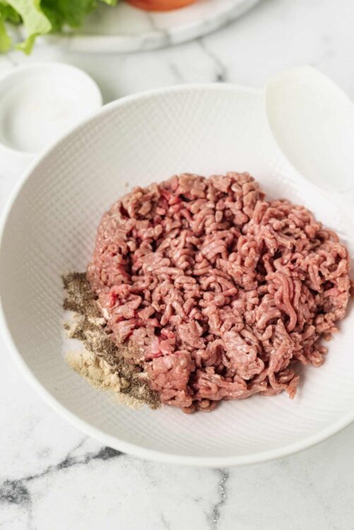 Ground beef in a white colander ready for cooking, with spices on the side. Perfect for making burgers, meatloaf, or chili.