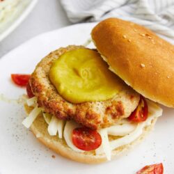 Crispy chicken sandwich with pickles, cherry tomatoes, and shredded cheese on a bun. Perfect comfort food recipe from Baked Bree.