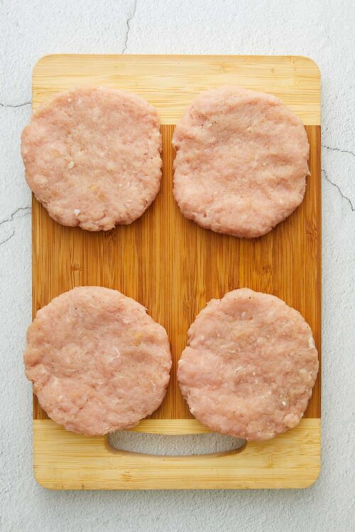 Breaded chicken patties ready for cooking on a wooden cutting board, perfect for homemade chicken sandwiches.