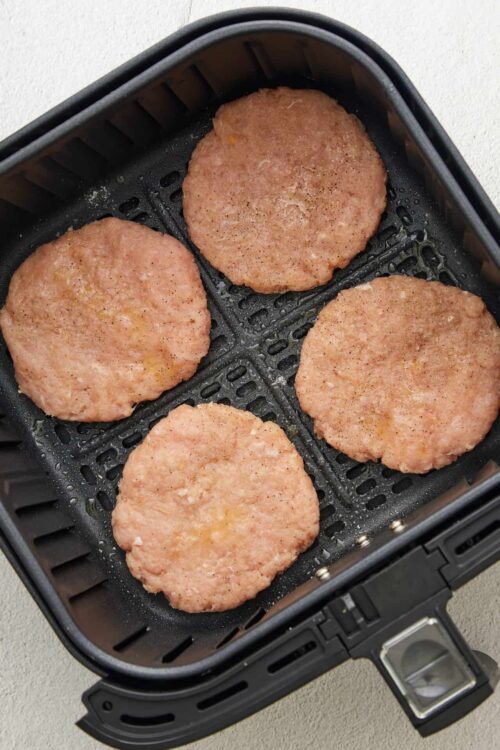 Crispy air fryer chicken patties cooking on black air fryer basket.