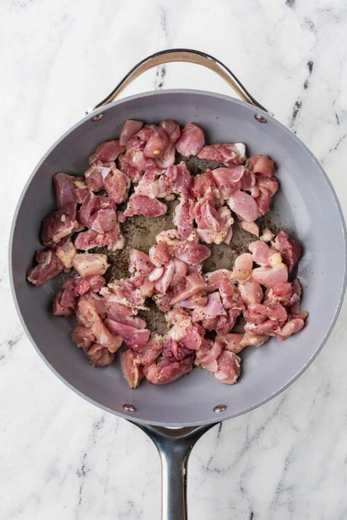 Diced raw chicken in a gray skillet for cooking or baking recipes.