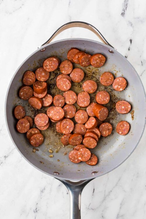 Sliced sausage links cooking in a gray skillet on a marble countertop.