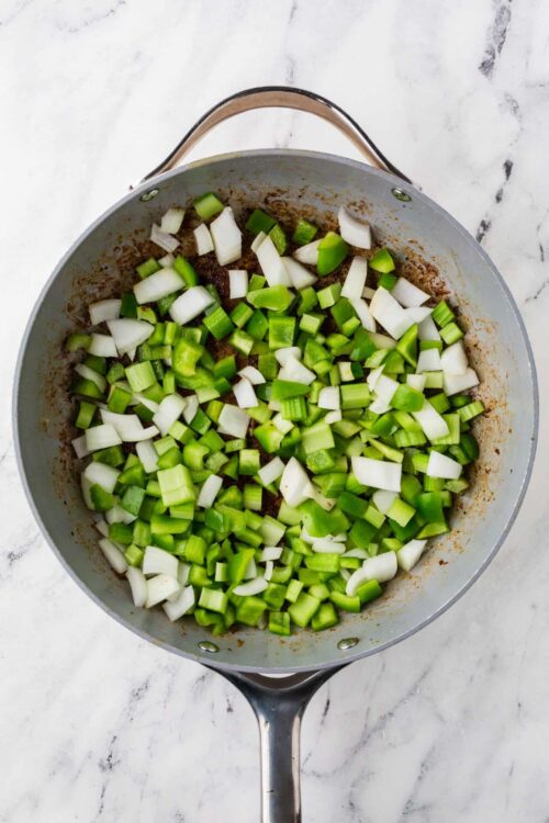 Sautéed chopped green onions in a skillet with browned edges on a white marble surface.