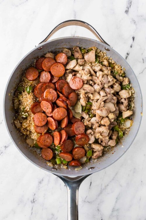 Sausage, rice, and chicken skillet meal in a round skillet on marble surface.