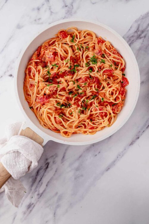 Creamy tomato pasta with fresh herbs served in a white bowl on marble surface.