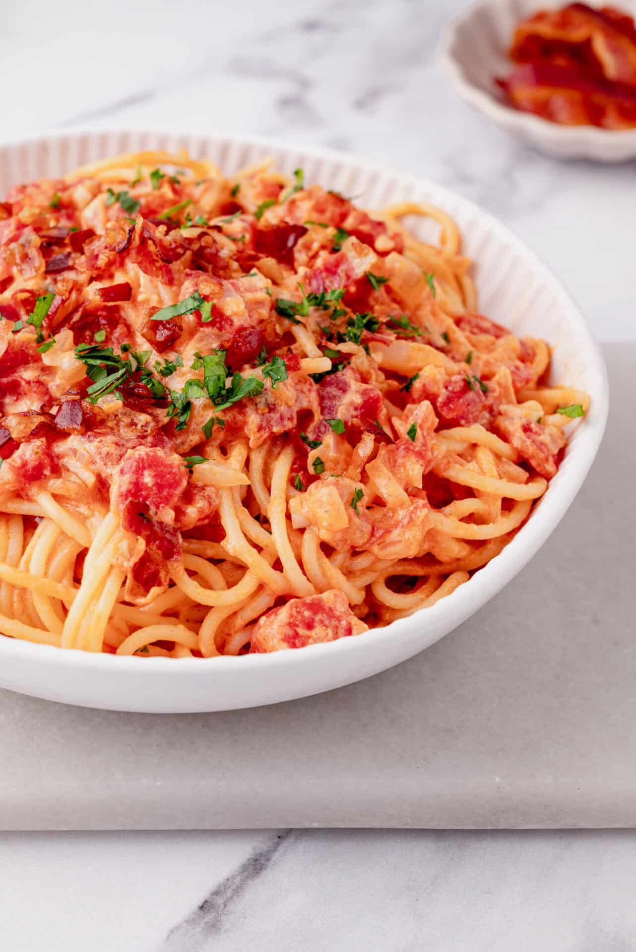 Creamy tomato bacon pasta dish served in a white bowl, garnished with fresh parsley.