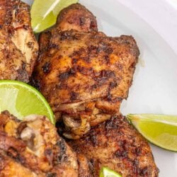Juicy roasted chicken thighs with crispy seasoned skin garnished with fresh lime wedges for flavor enhancement.