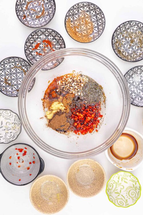 Spice mix in a glass bowl surrounded by patterned spice jars on a white background.
