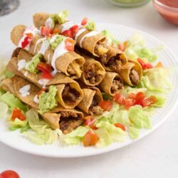 Crispy beef tacos with lettuce and tomato on white plate.