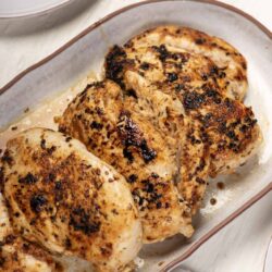 Juicy roasted chicken breasts with crispy, seasoned skin in a baking dish.