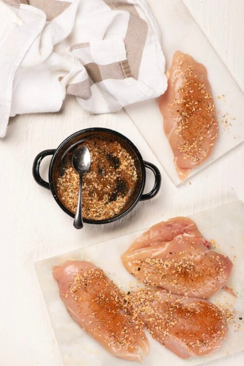 Seasoned chicken breasts with spices and breadcrumb mixture on parchment paper.