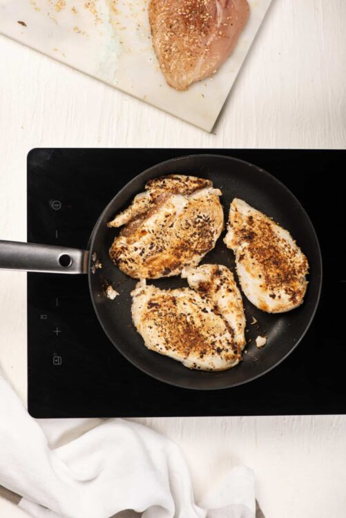 Juicy seasoned chicken breasts cooking in a black skillet on a white countertop.