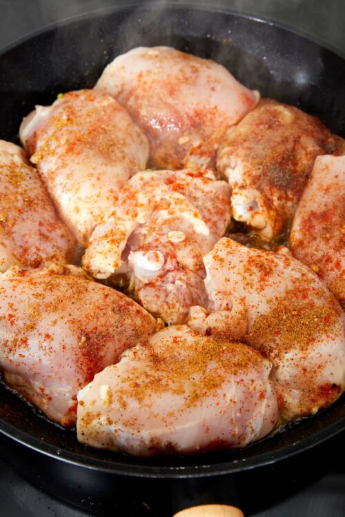 Seasoned chicken thighs cooking in a skillet with paprika and spices for flavorful baked chicken recipes.