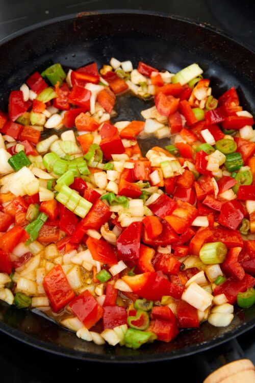 Chopped bell peppers and green onions sautéing in a skillet for a flavorful vegetable stir-fry.