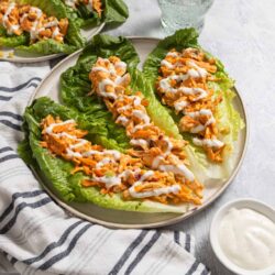 Baked chicken lettuce wraps with drizzled sauce on a white plate.