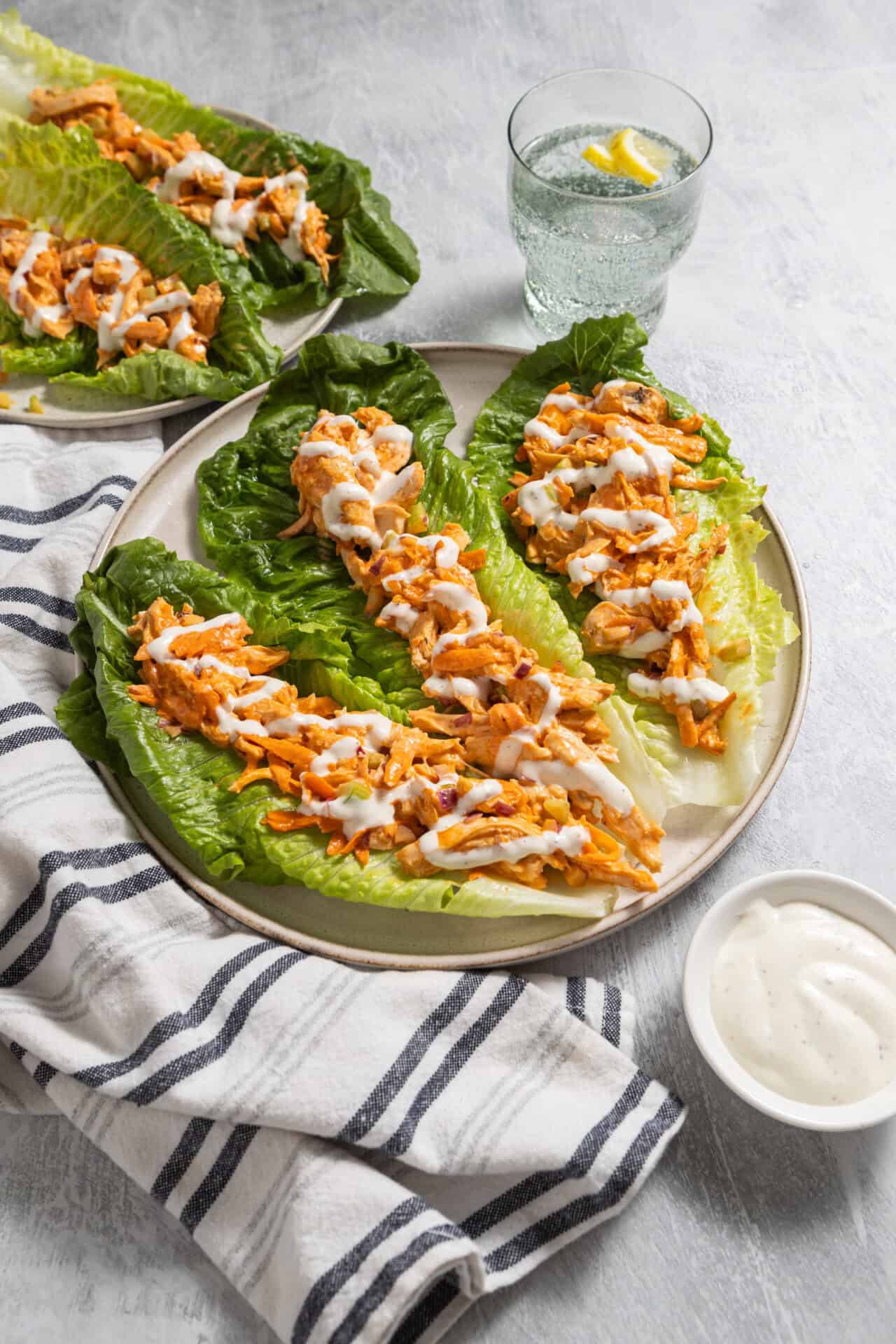 Baked chicken lettuce wraps with drizzled sauce on a white plate.