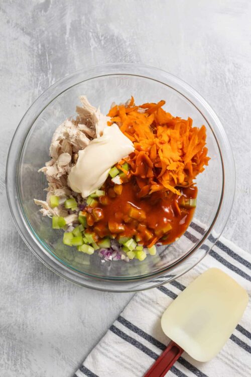 Chopped cooked chicken, shredded carrots, celery, cream cheese, and BBQ sauce in a glass mixing bowl.
