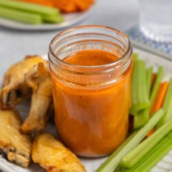 Fresh buffalo chicken wing sauce with celery and carrots on a white plate close-up.