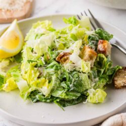 Fresh Caesar salad with crunchy croutons and grated cheese on a white plate.