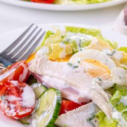 Fresh chicken salad with eggs, cucumbers, and tomatoes on a white plate, served with creamy dressing.