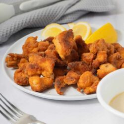 Crispy fried chicken bites served with lemon wedges and dipping sauce on a white plate.