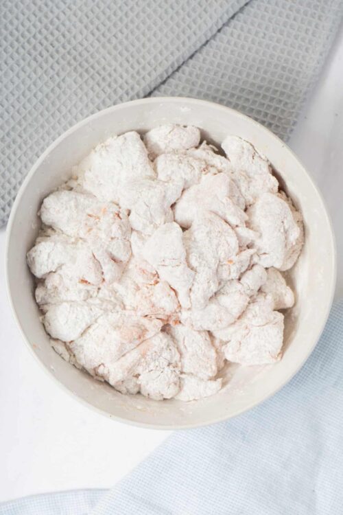 Flour-coated chicken pieces in a white bowl for baking or frying.