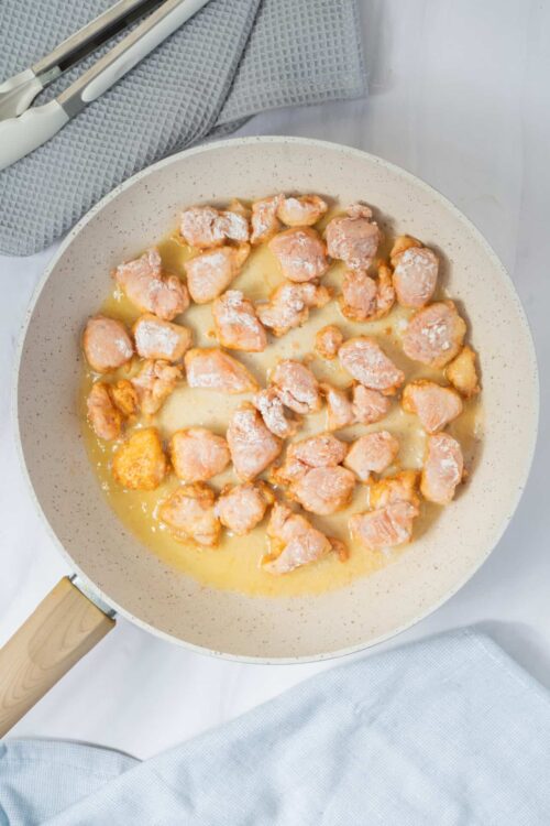 Juicy raw chicken chunks sizzling in a white skillet for cooking recipes.