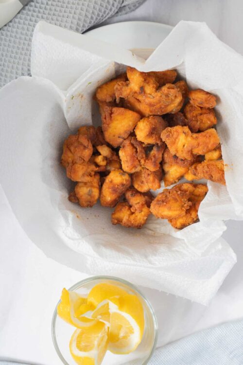 Crispy fried chicken tenders served on paper towels for extra crunch, with a side of lemon slices for a fresh flavor.