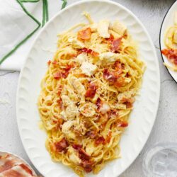 Creamy chicken carbonara pasta on an elegant white serving platter with bacon and cheese garnish.