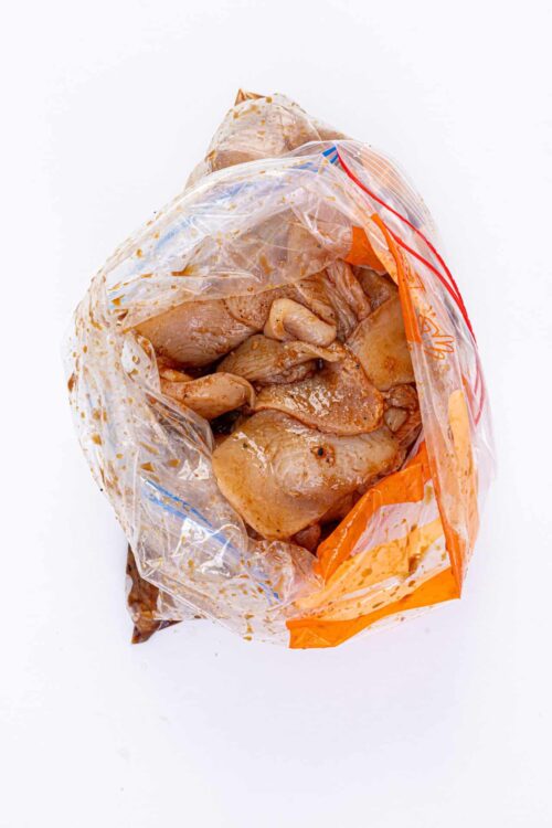 Marinated raw chicken in plastic bag on white background.