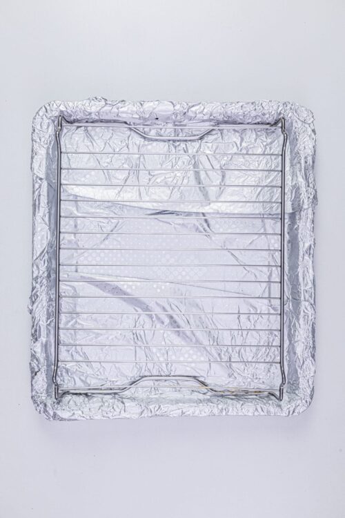 Aluminum foil-lined baking sheet with cooling rack on top, used for baking and cooling baked goods.