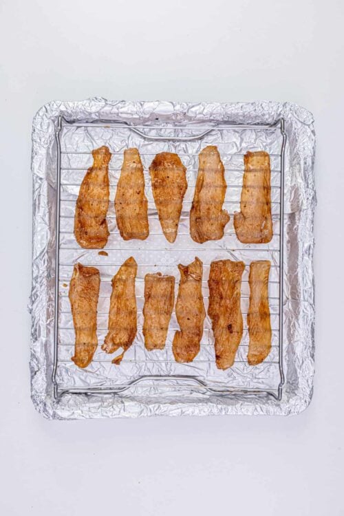 Crispy homemade bacon strips on baking rack, baked bacon on aluminum foil, easy bacon recipe, baked bree culinary website, breakfast meat essentials.